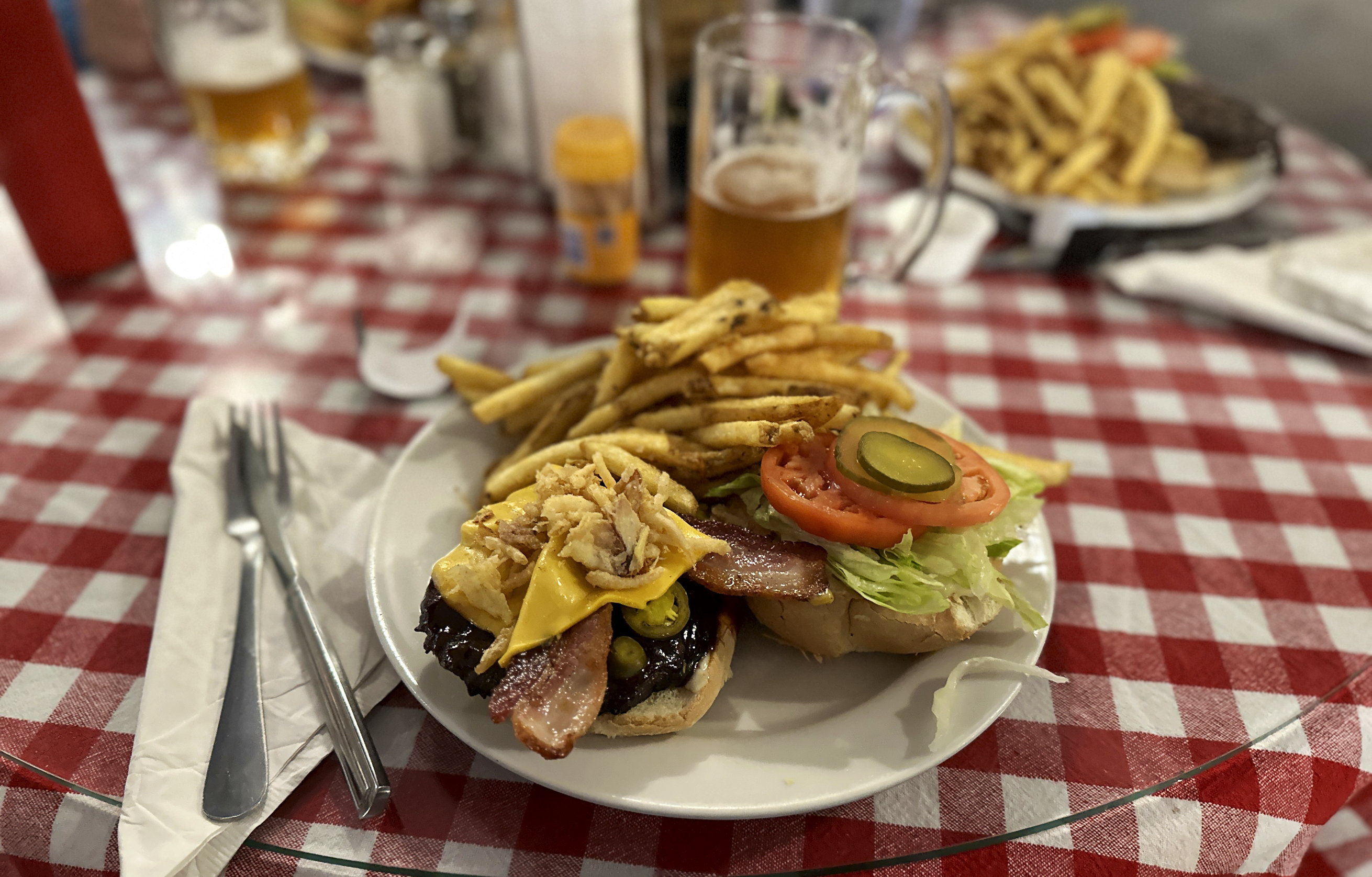 Ein Teller mit einem grossen Burger und Pommes steht auf dem rot/weiss karierten Tischtuch