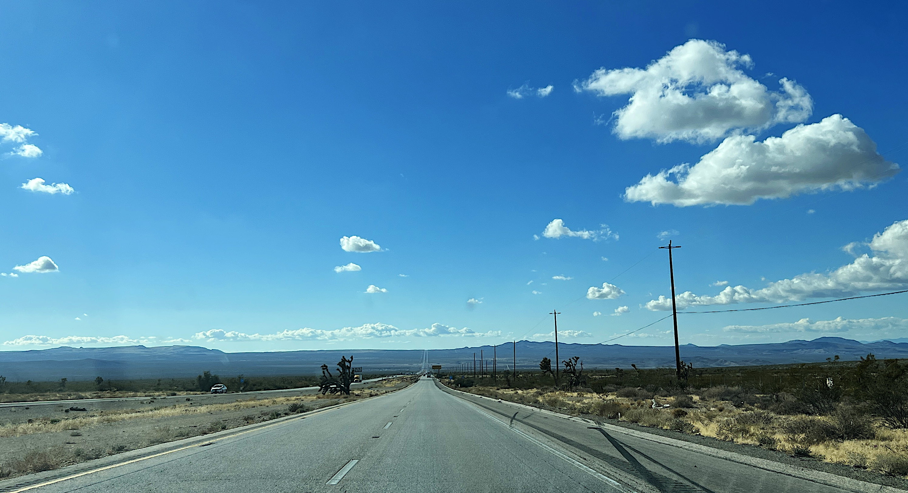 Die pro Richtung zweispurige Autobahn führt bis zum Horizont geradeaus. Der blaue Himmel ist mit ein paar Wattebäuschen verziert.