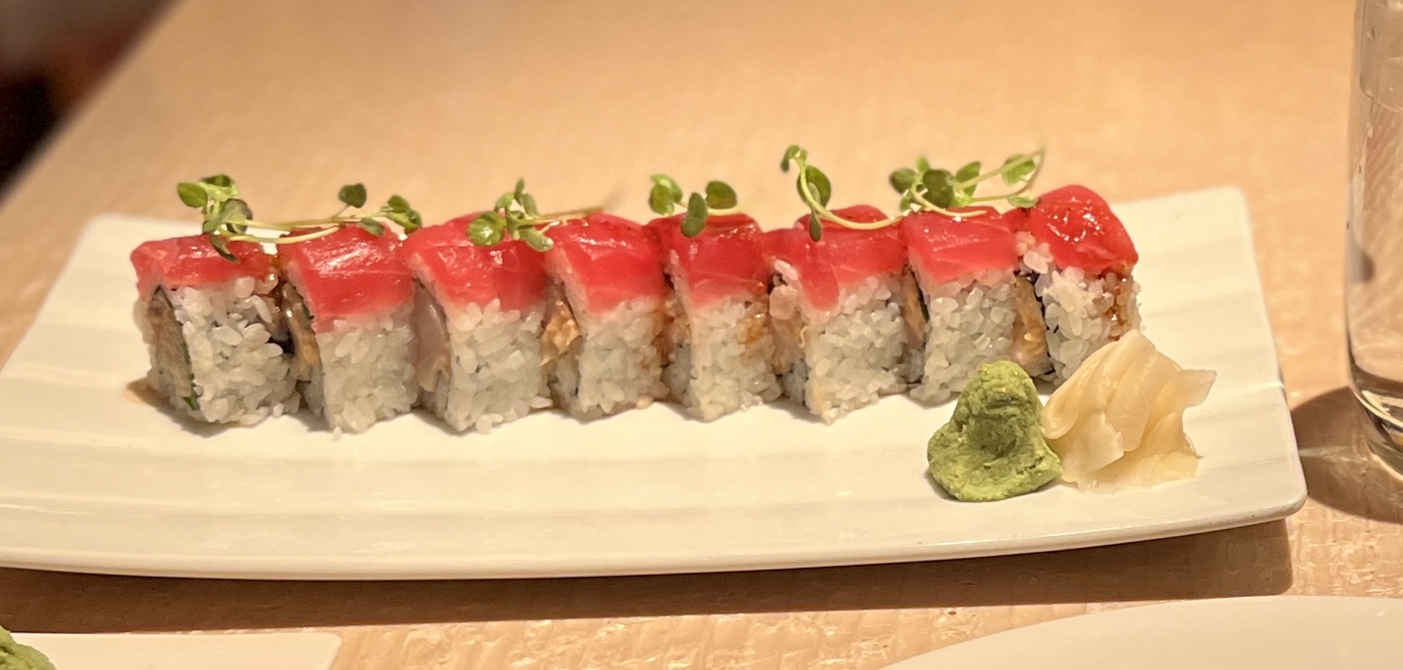 Ein länglicher, schmaler Teller mit ach Stückchen einer Sushi-Rolle mit Thun. Schön dekoriert mit ein wenig Kresse. Dazu Ingwer-Scheibchen und ein Klacks Wasabi.