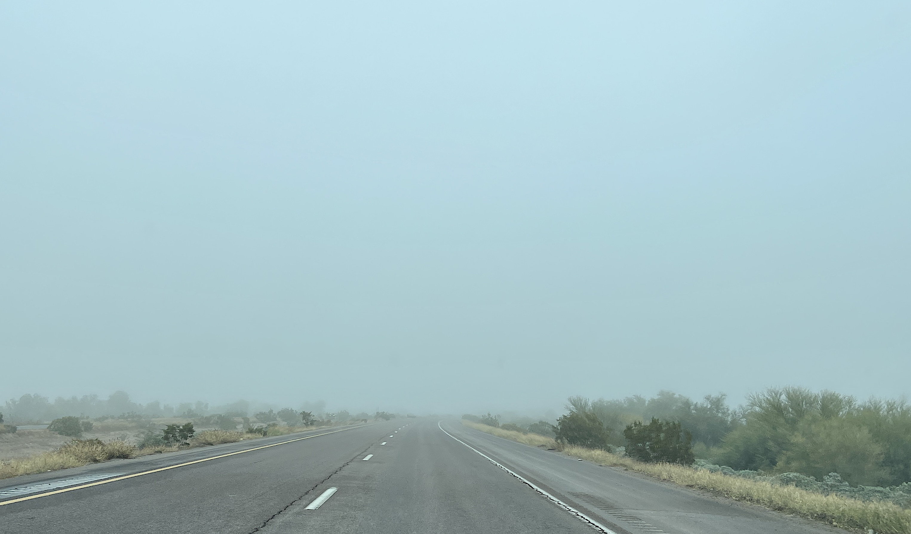 Eine zweispurige Autobahn führt geradeaus in den Nebel. Links und rechts Büsche und Steppe.