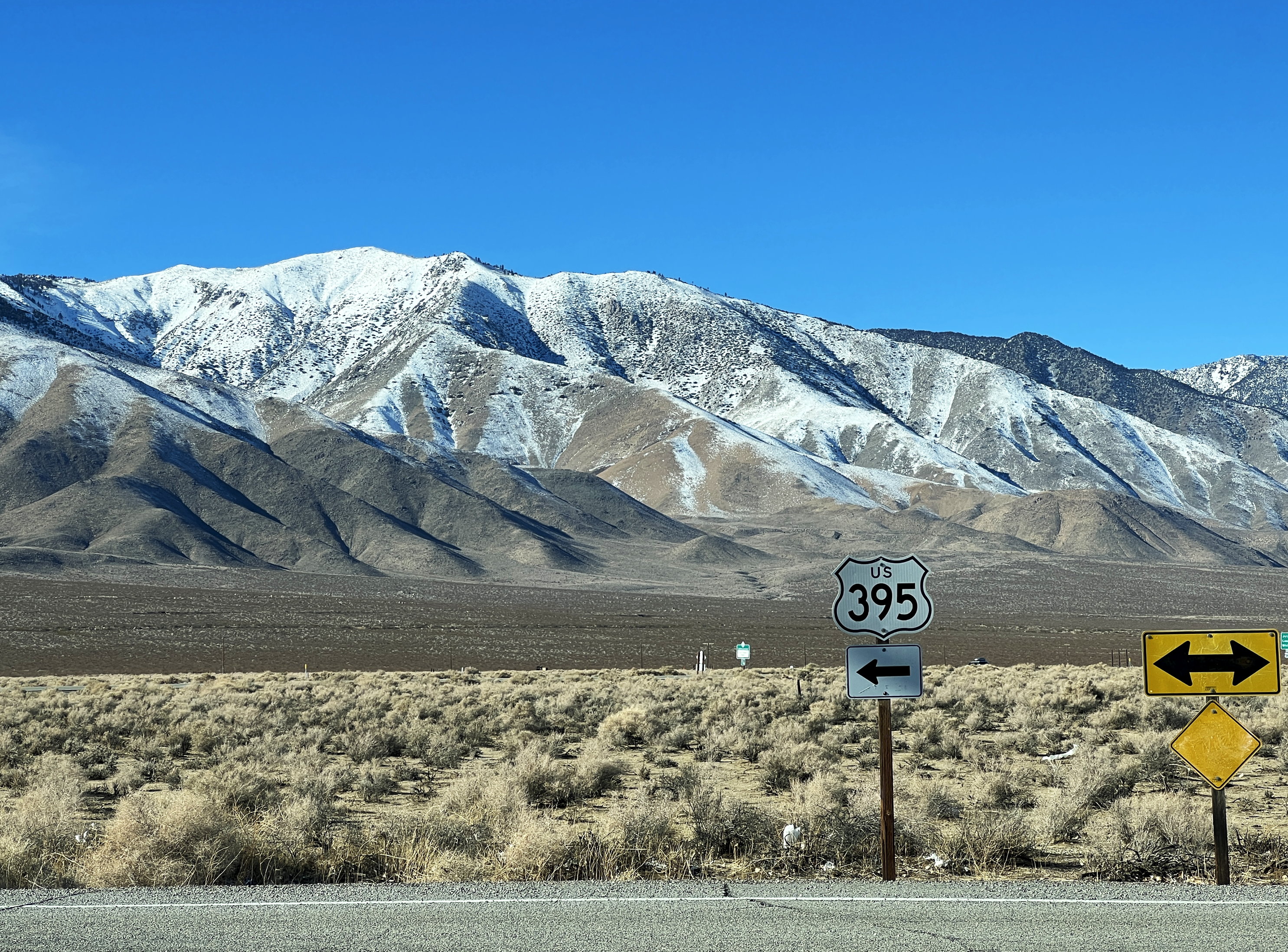 Strassenschild California Highway 395, dahinter die schneebedeckten Berge der Sierra Nevada