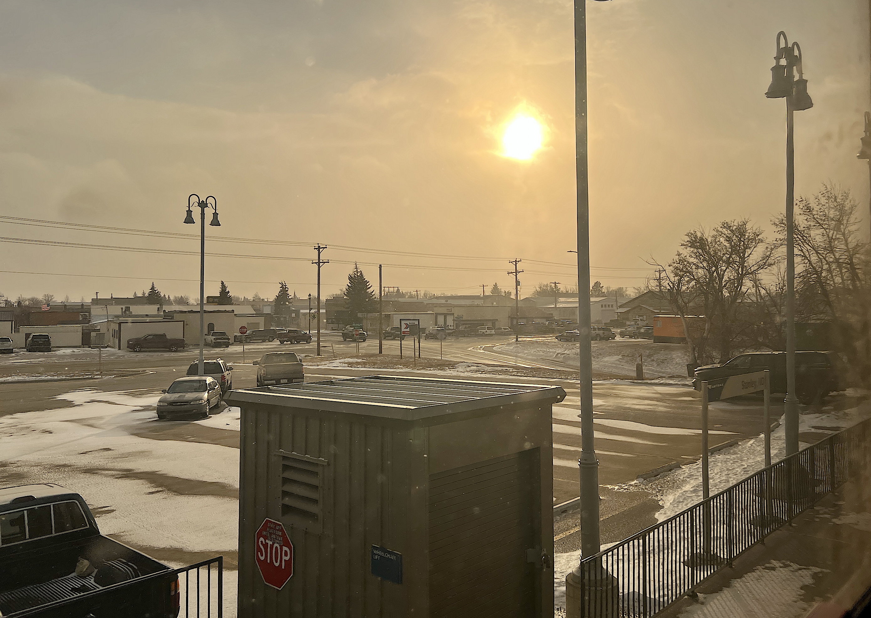 In Stanley, North Dakota, der halbe Bahnsteig ist sichtbar, dahinter die Kurzzeitparkplätze. Der Himmel ist beinahe gelblich, Schneeschauer trüben das Bild