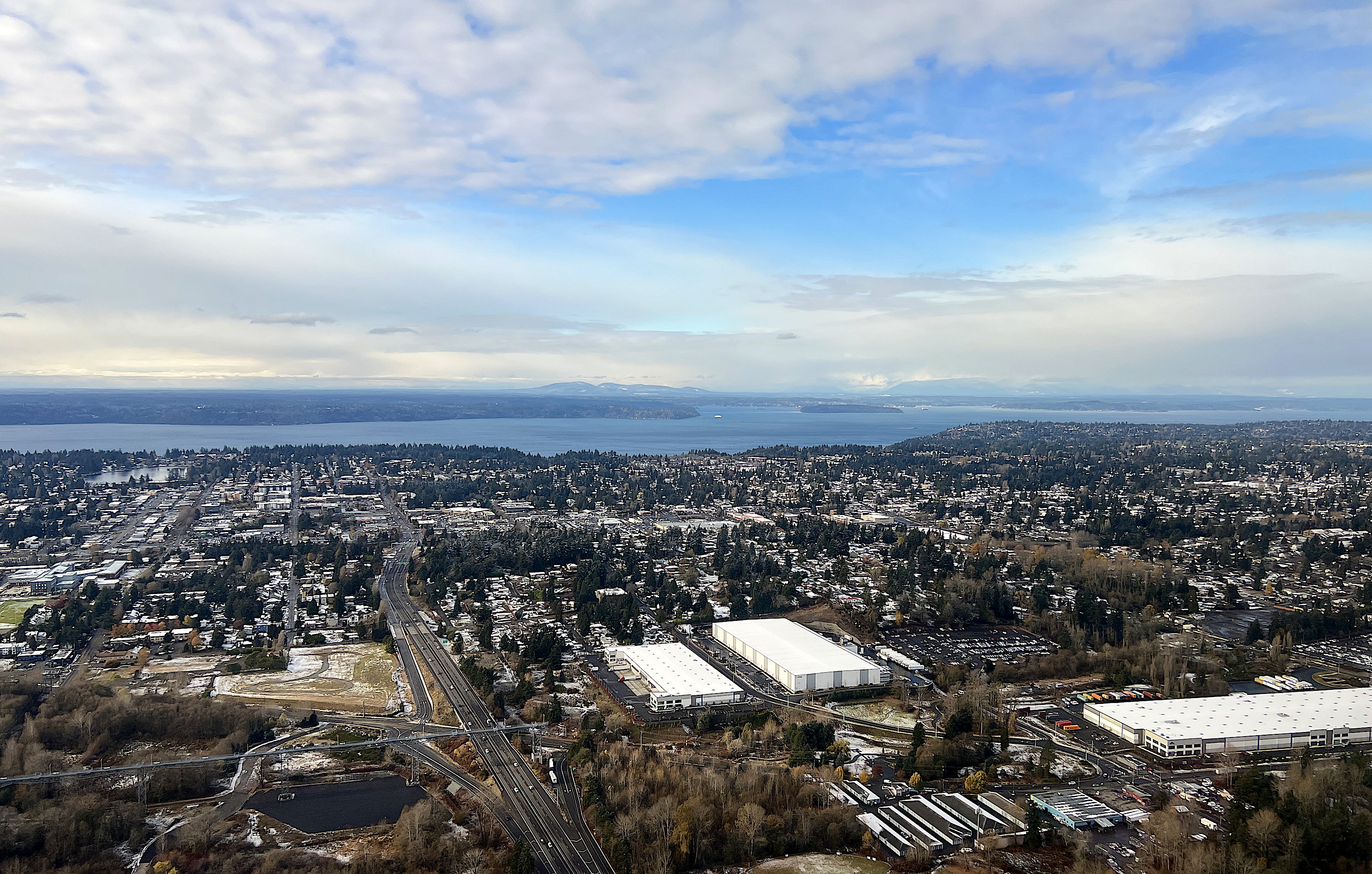 Blick aus dem eben gestarteten Flugzeug über die Bucht vor Seattle. Vorne viele Häuschen und eine grosse Autobahn.