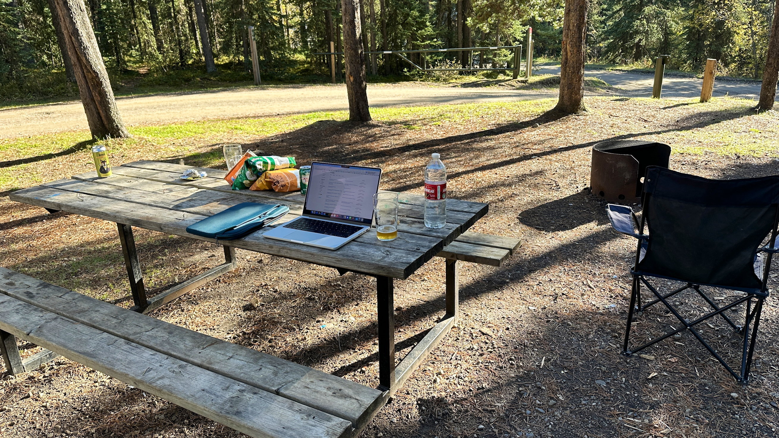 Ein Holz-Campingtisch mit Laptop, Chips und Wasserflasche