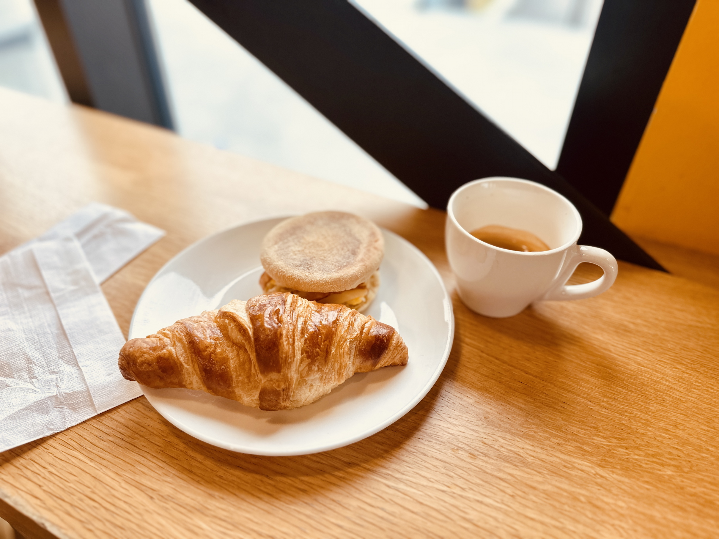 Teller mit Croissant und einem English Muffin, daneben eine Tasse Kaffee