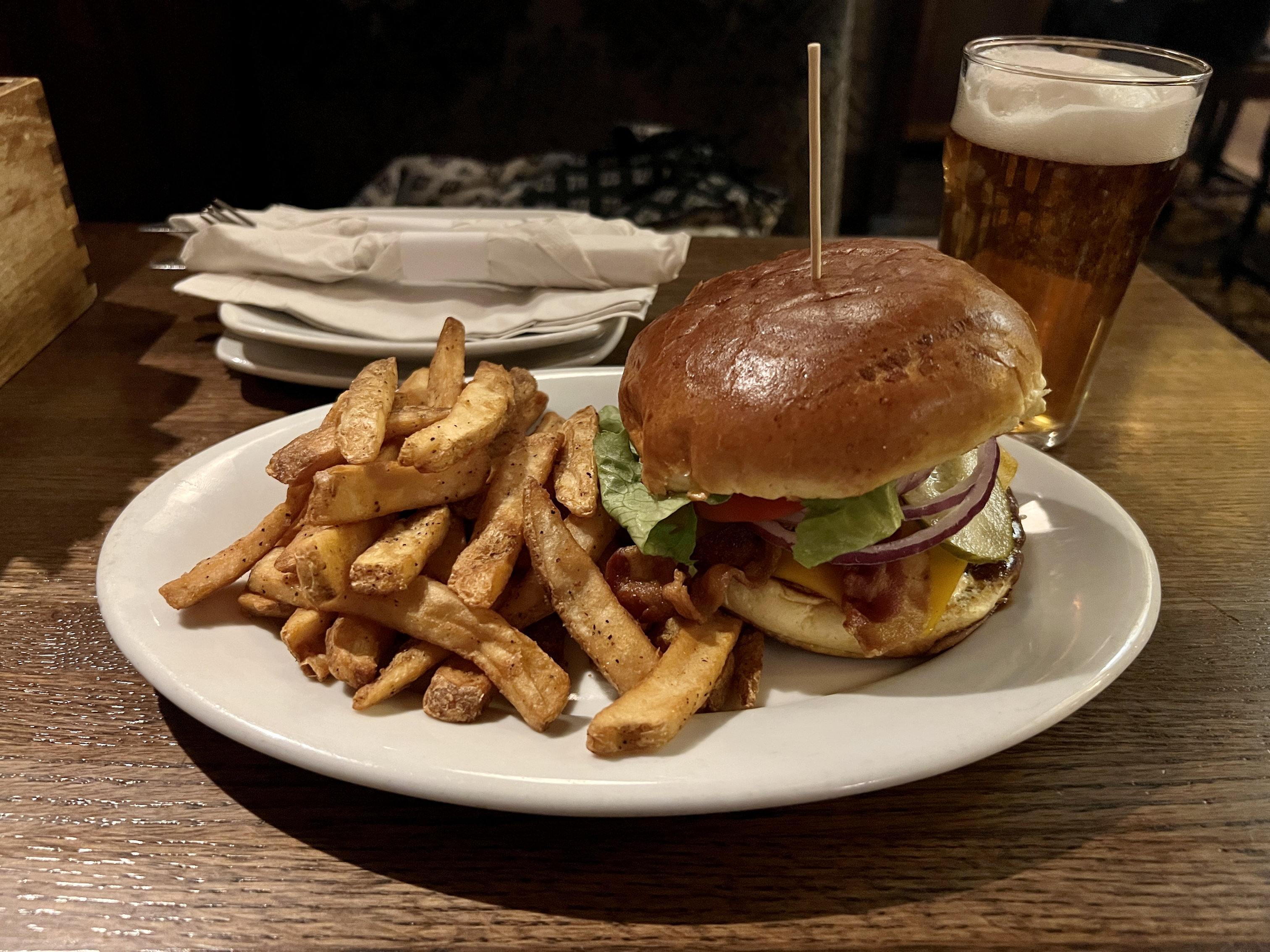 Ein Teller mit einer ordentlichen Portion Pommes und einem grossen Burger. Dahinter ein Glas Bier
